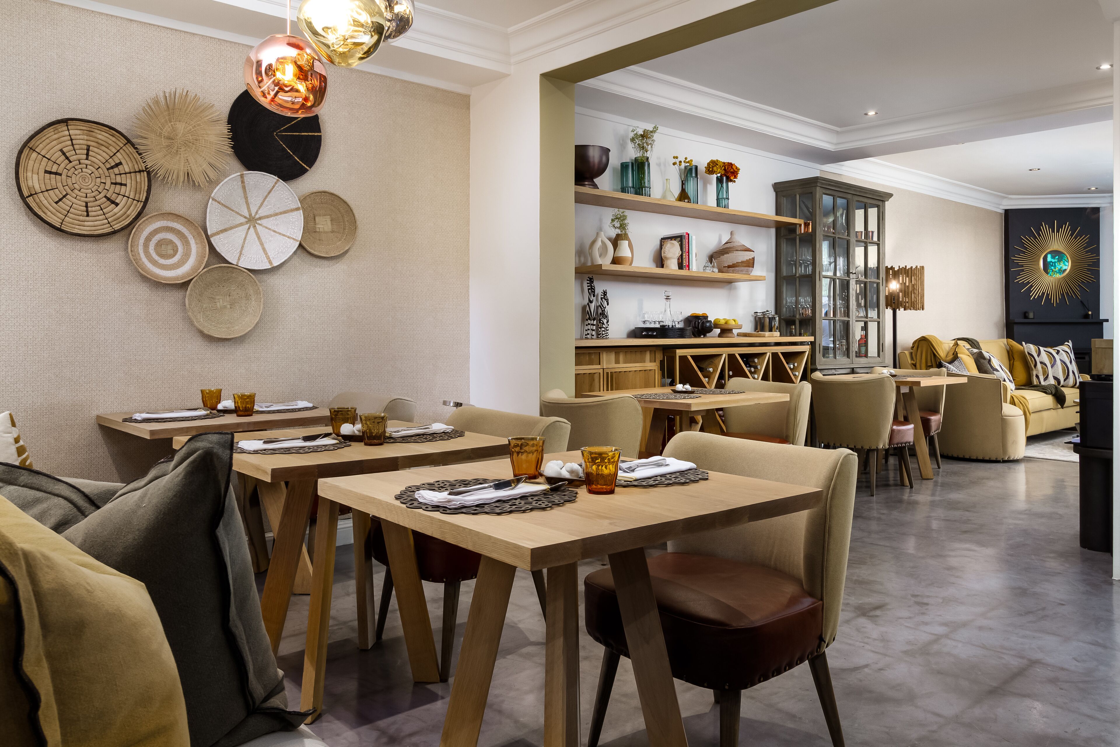 Un espace de restauration moderne avec des tables et des chaises en bois, une variété d’œuvres d’art décoratives murales et un coin salon confortable agrémenté de coussins.