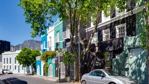 A street with a parked silver car, buildings with balconies, and a mountain in the background. - Cape Finest Guesthouse (Cape Town)
