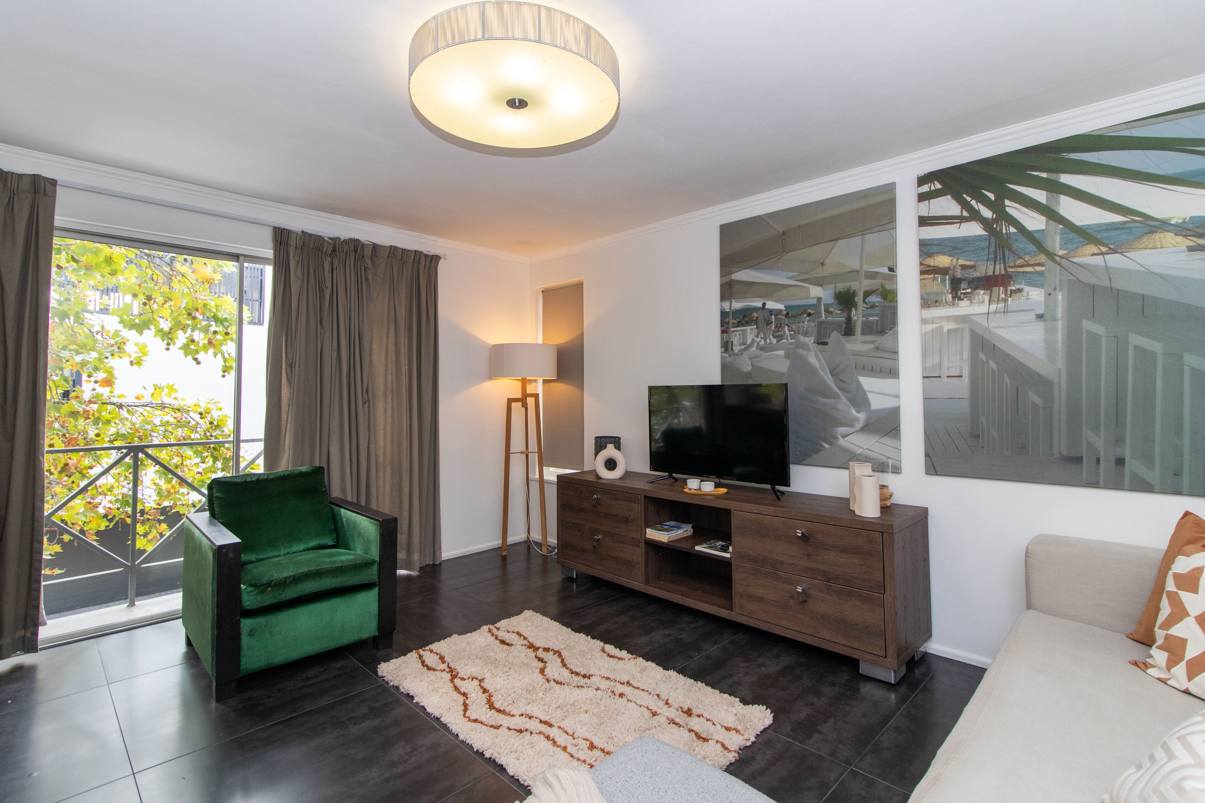 Una sala de estar moderna con un sillón verde, un televisor sobre un mueble de madera y un ventanal que da a un balcón.