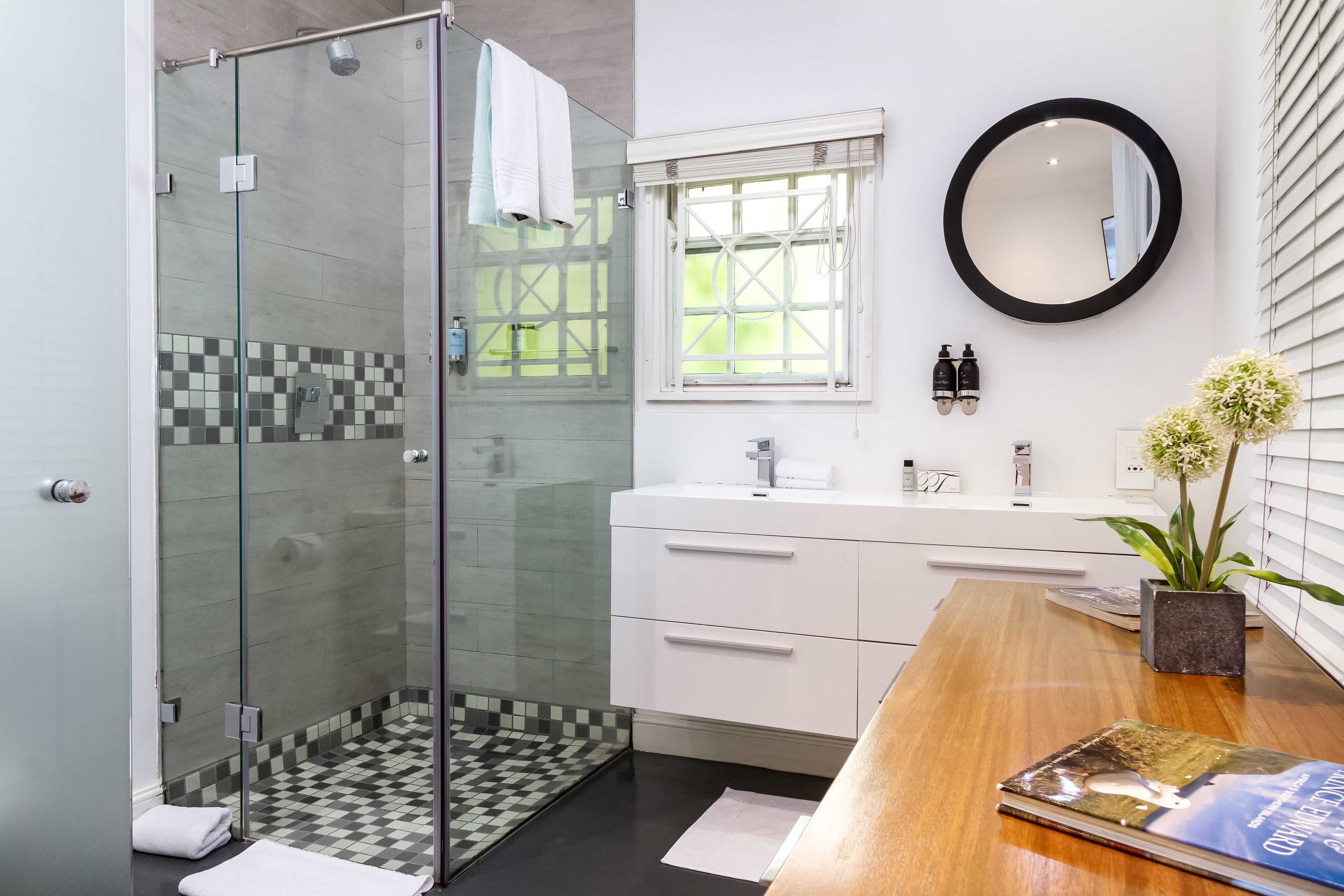A modern bathroom with a glass-enclosed shower, a wooden vanity with a mirror, and a checkered floor.