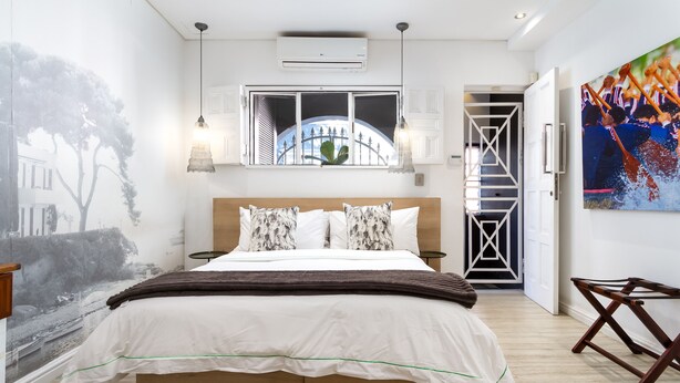 A bedroom with a large bed, a window with a view of a bridge, a painting on the wall, and a door leading to a staircase. - Cape Finest Guesthouse (Cape Town)