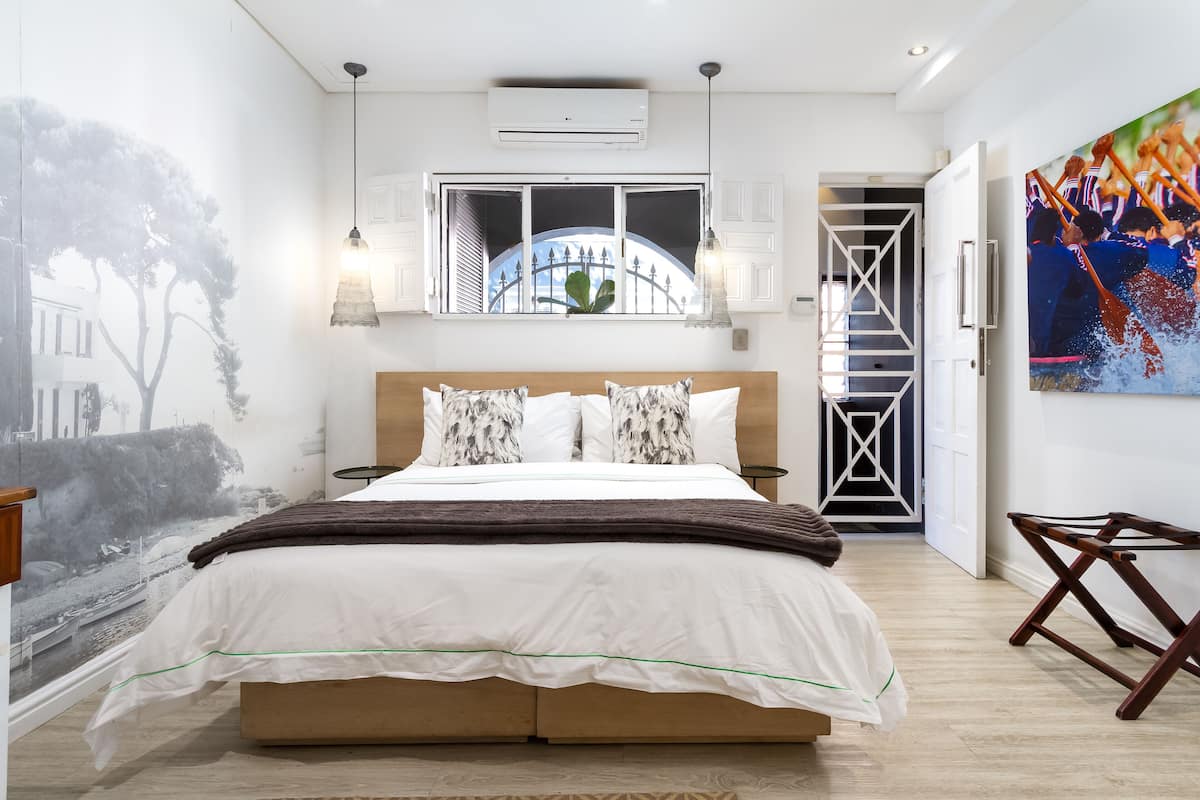 Um quarto com uma cama grande, uma janela com vista para uma ponte, um quadro na parede e uma porta que dá para uma escadaria.