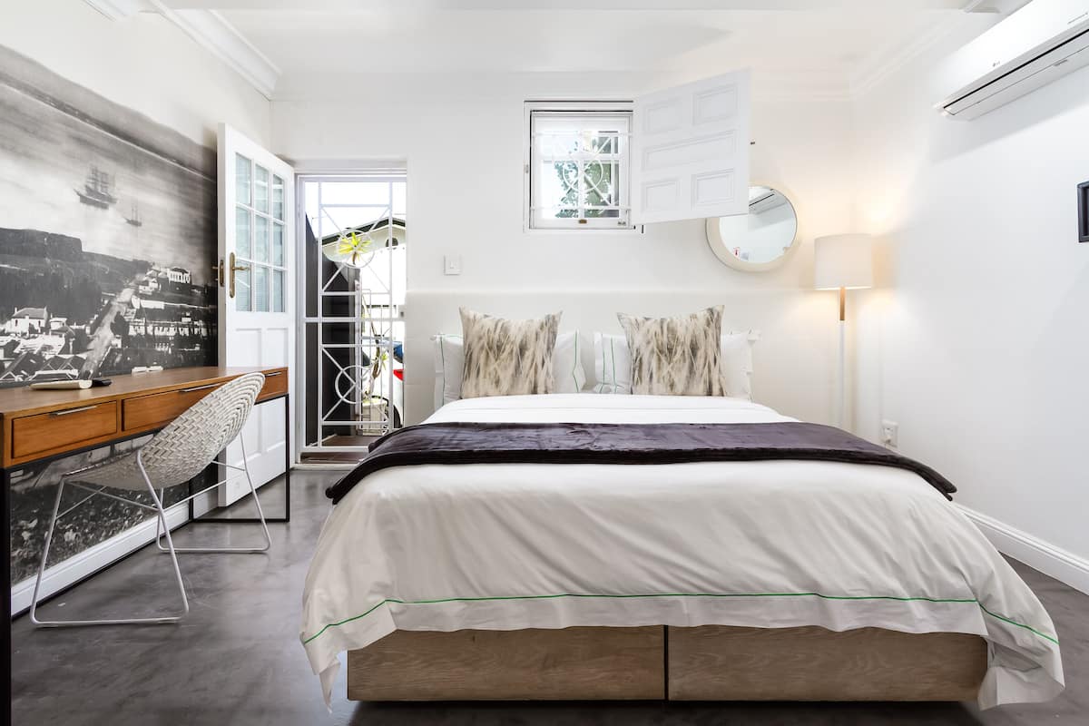 Quarto com cama, escrivaninha e cadeira. Janela com vista para o exterior.