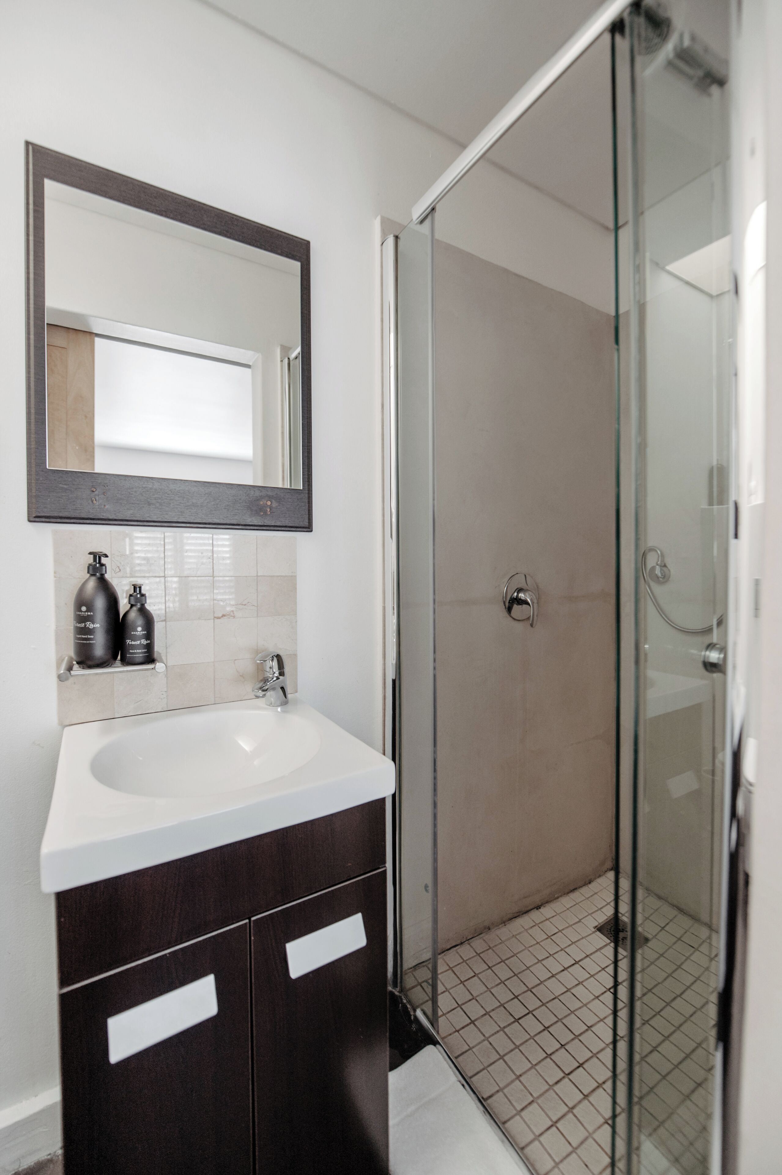 A bathroom with a white sink, dark wooden cabinets, a large mirror, and a glass shower enclosure.
