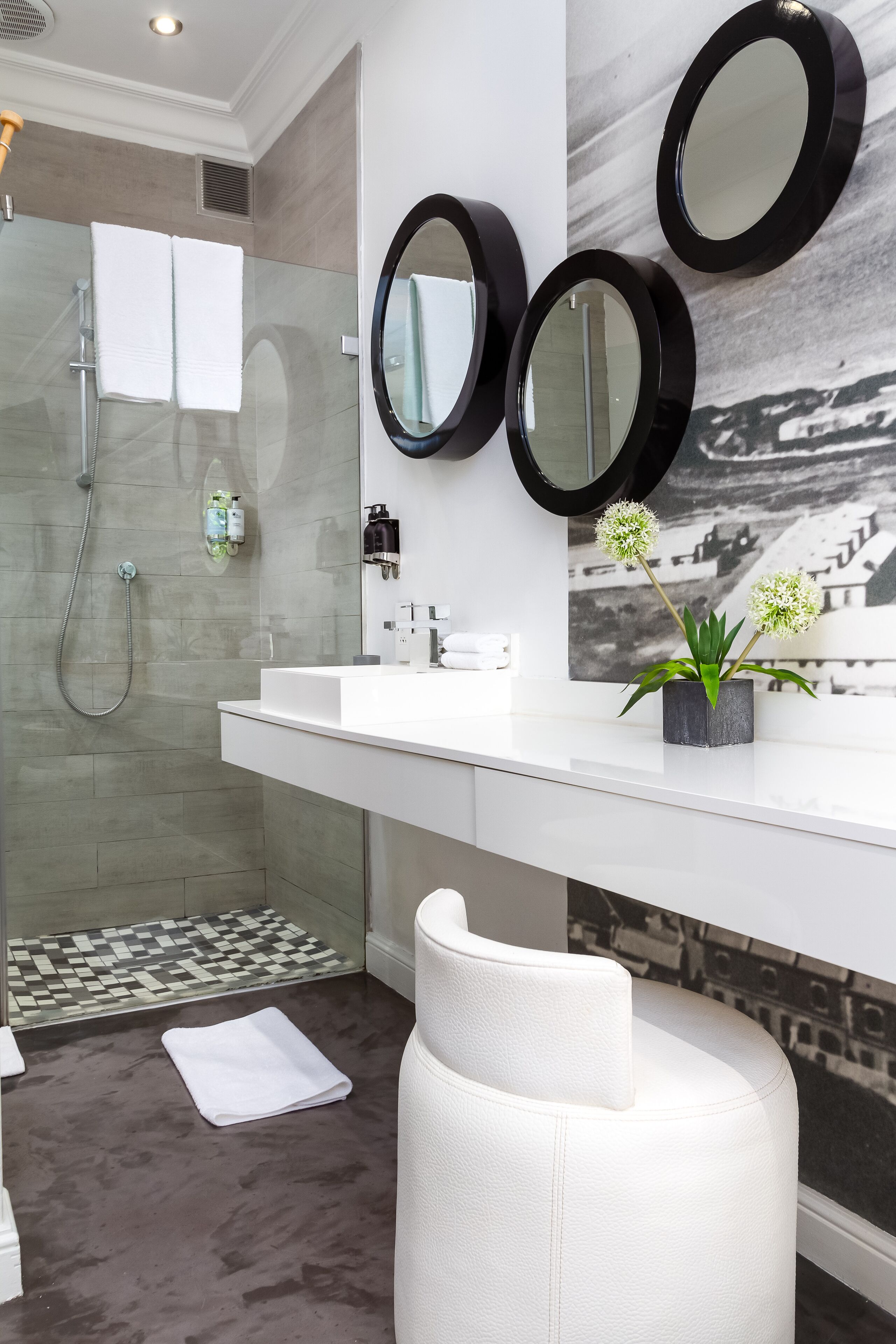 A modern bathroom with a glass-enclosed shower, white vanity, and three round mirrors.