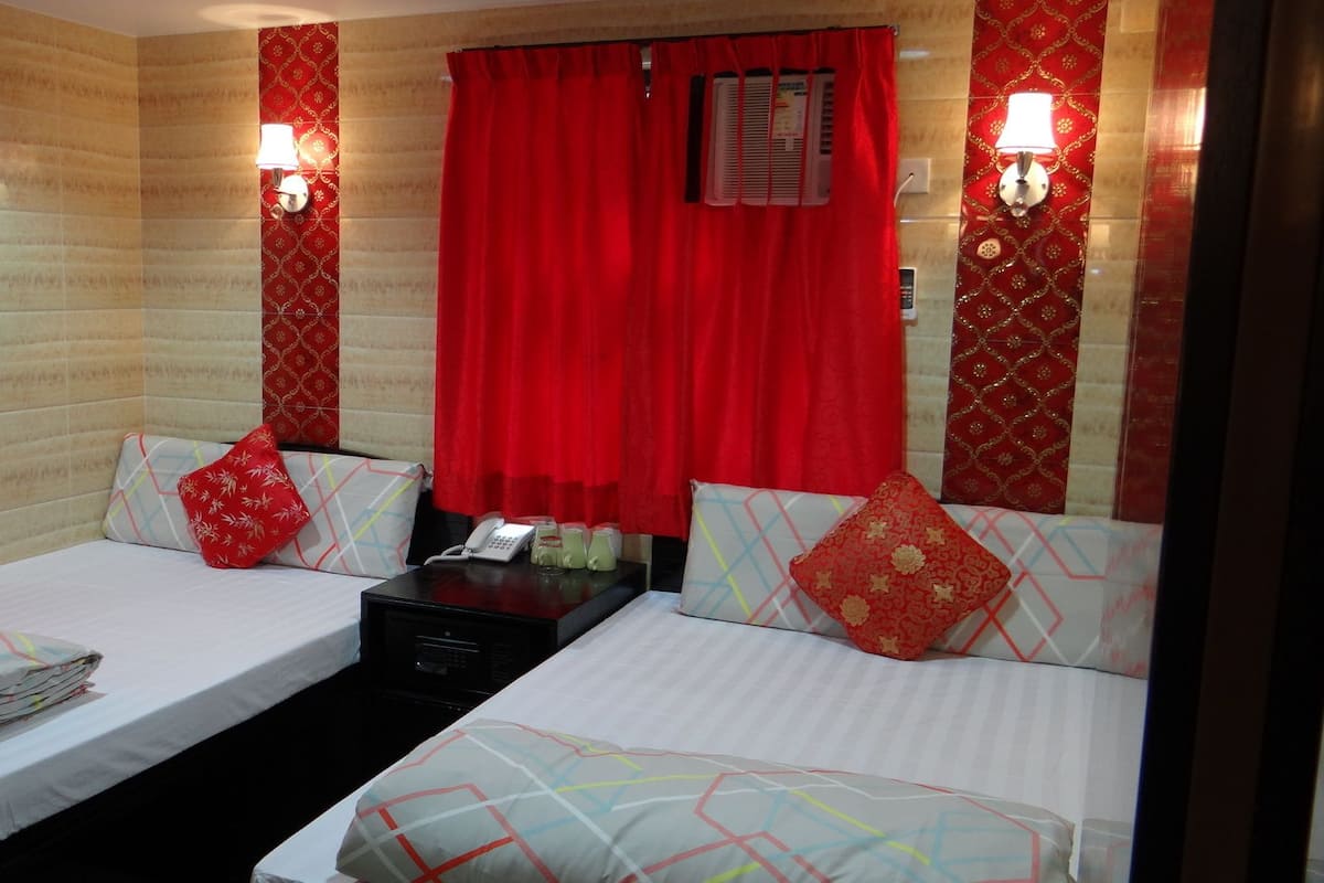 A hotel room with two beds, red curtains, patterned wall decor, and bedside lamps.