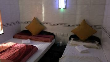 A small, dimly lit hotel room with two single beds, each with a pillow and a blanket.