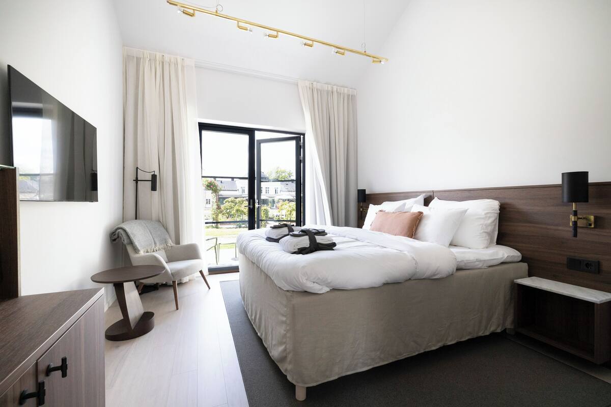 A modern hotel room with a large bed, a desk, a chair, and a TV.