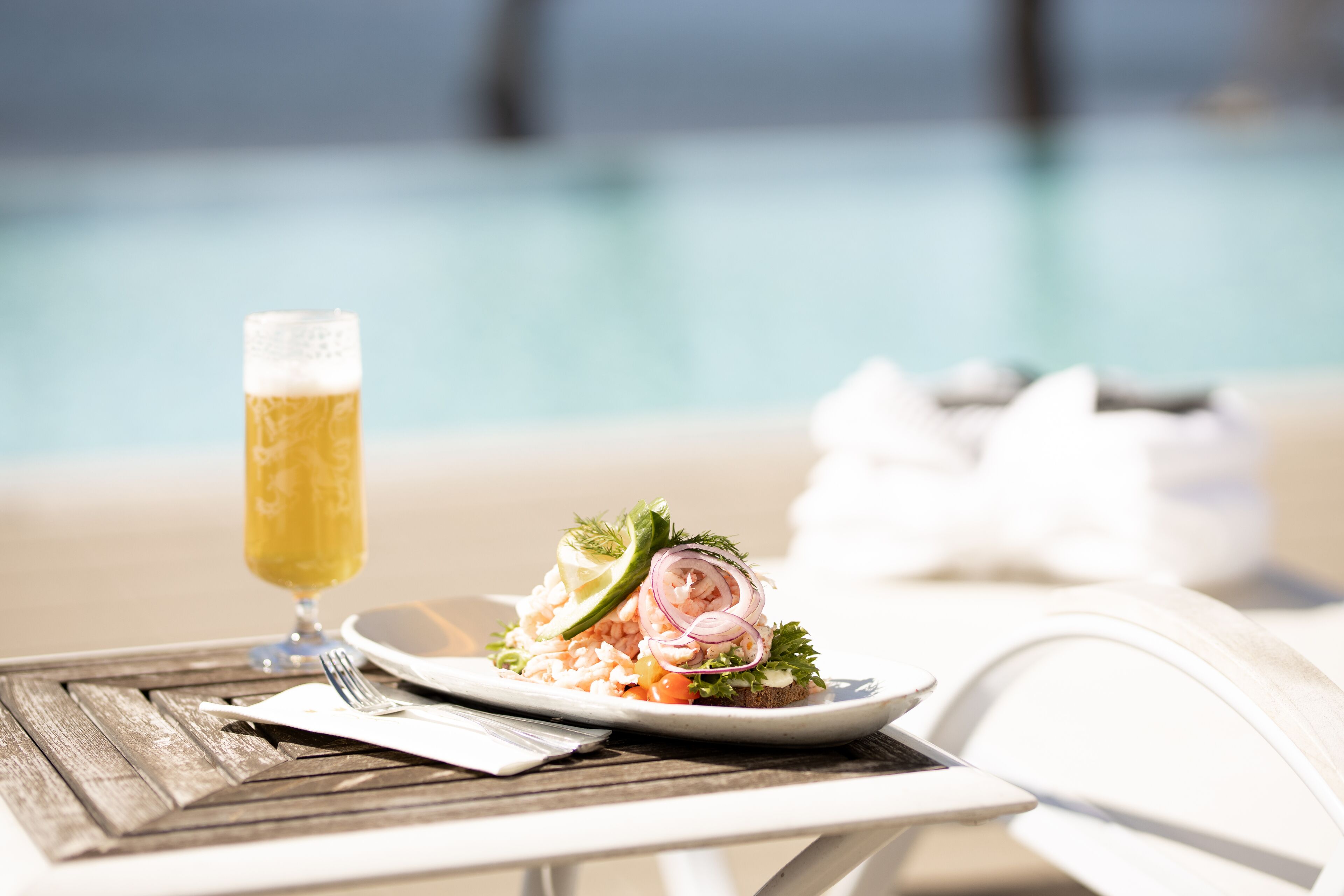 Una mesa de comedor con un plato de comida y una jarra de cerveza, cerca de una piscina.