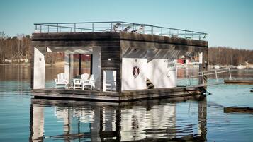 Una casa flotante con zona de terraza, un flotador salvavidas y un letrero que dice 'Beach House'.