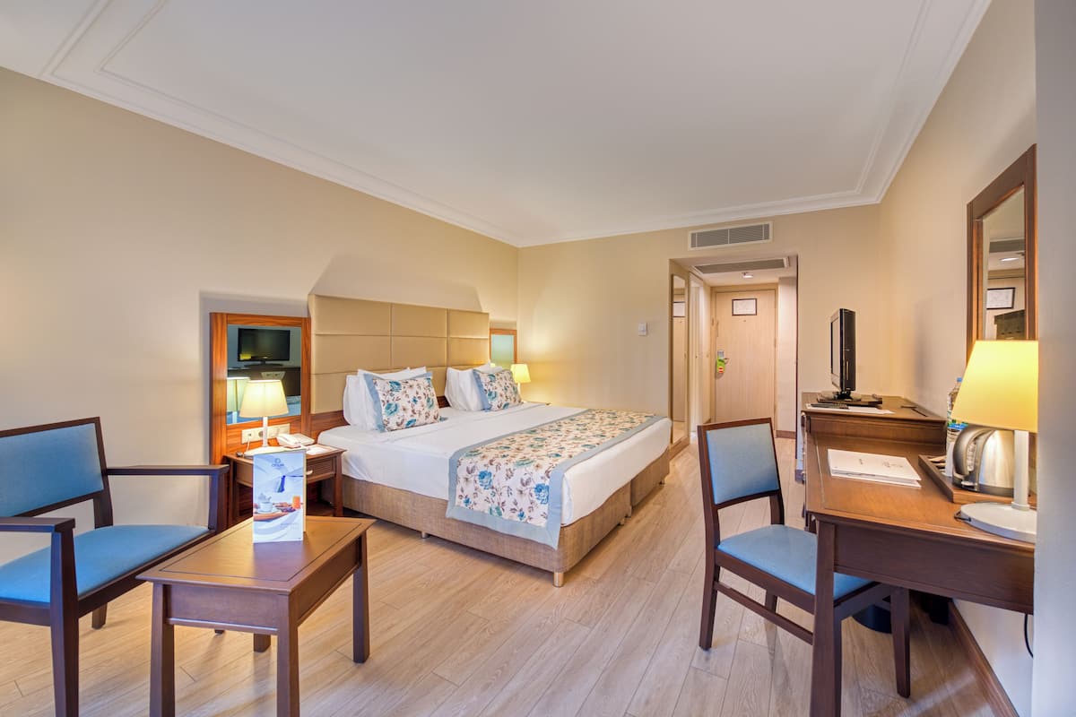 Une chambre d’hôtel avec un lit, deux chaises, un bureau, une lampe et un téléviseur.