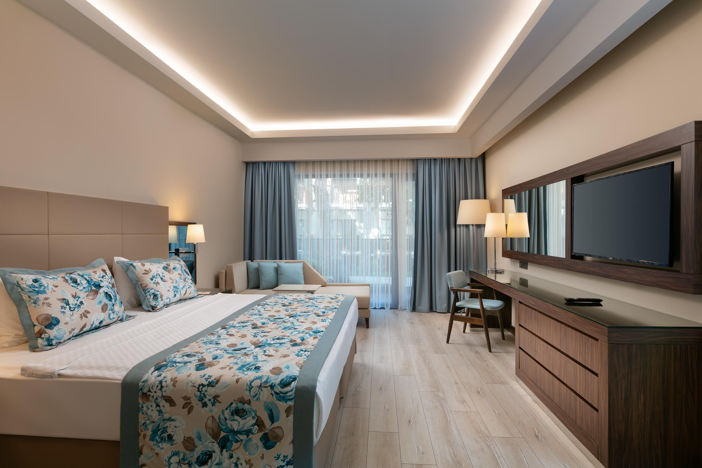 Une chambre d’hôtel moderne dotée d’un grand lit, d’un bureau, d’une télévision et offrant une vue sur la ville grâce à de grandes fenêtres.
