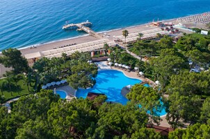 Vista aérea de un resort con una gran piscina, un muelle que se extiende hacia el mar y una zona de playa con sombrillas y tumbonas.