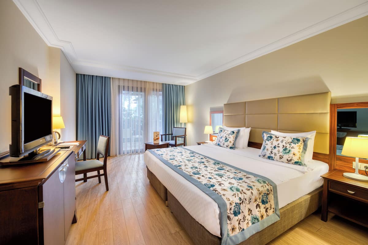 Une chambre d’hôtel avec un grand lit, un bureau avec une télévision, une chaise et une fenêtre avec des rideaux.
