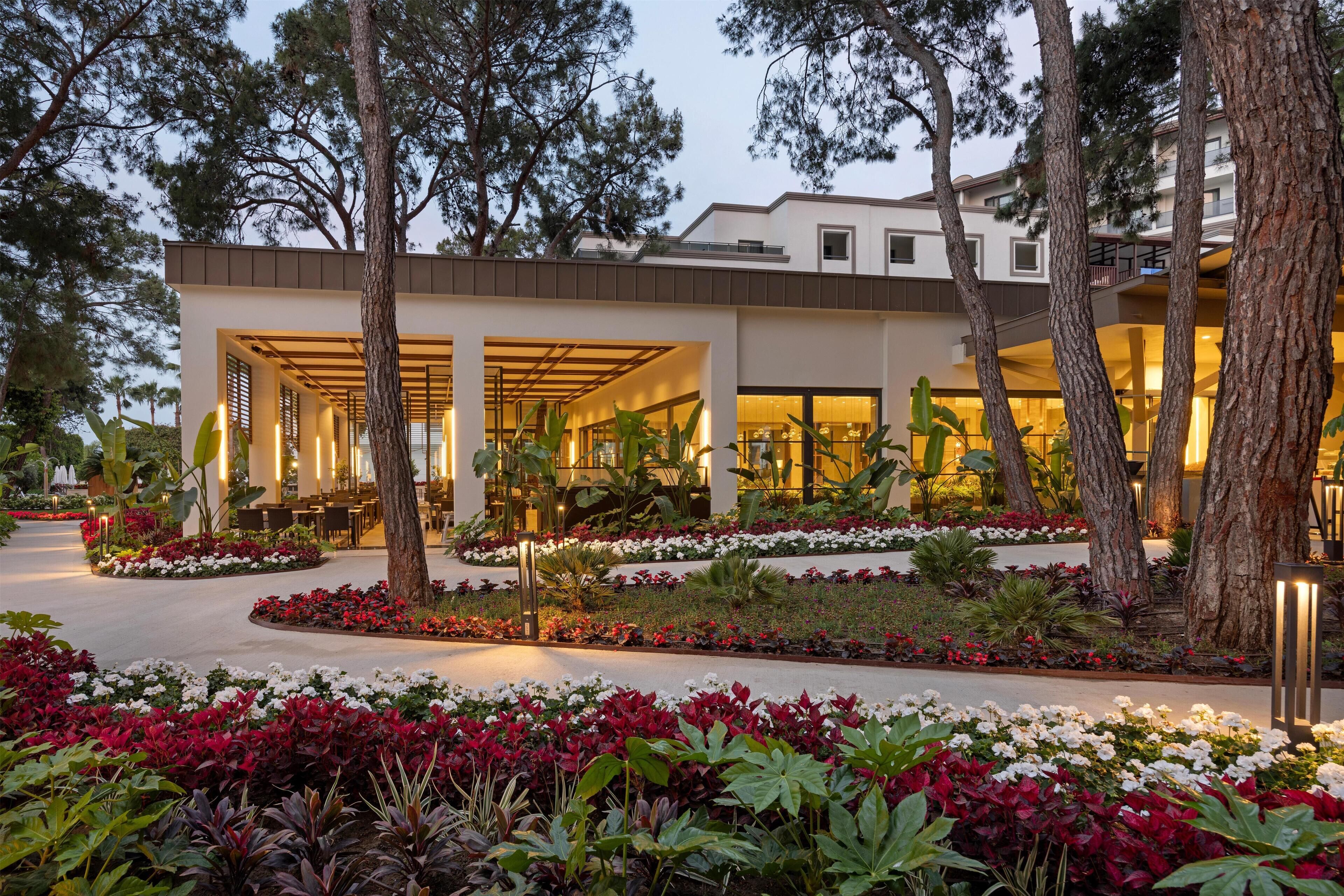 A modern hotel with a covered outdoor area, surrounded by landscaped gardens and trees.