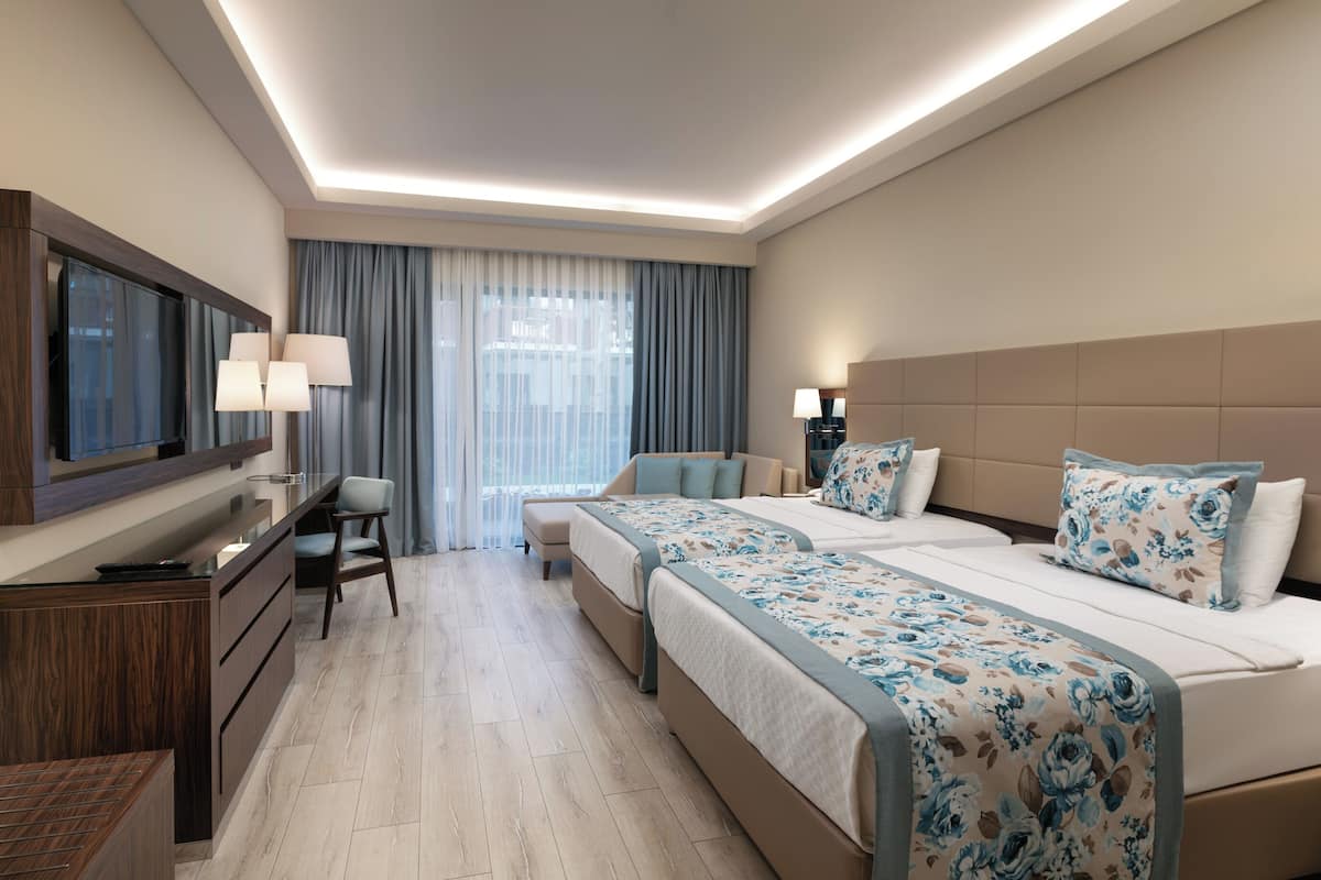 Une chambre d’hôtel avec un grand lit, un bureau avec une chaise, une télévision et une fenêtre avec des rideaux.