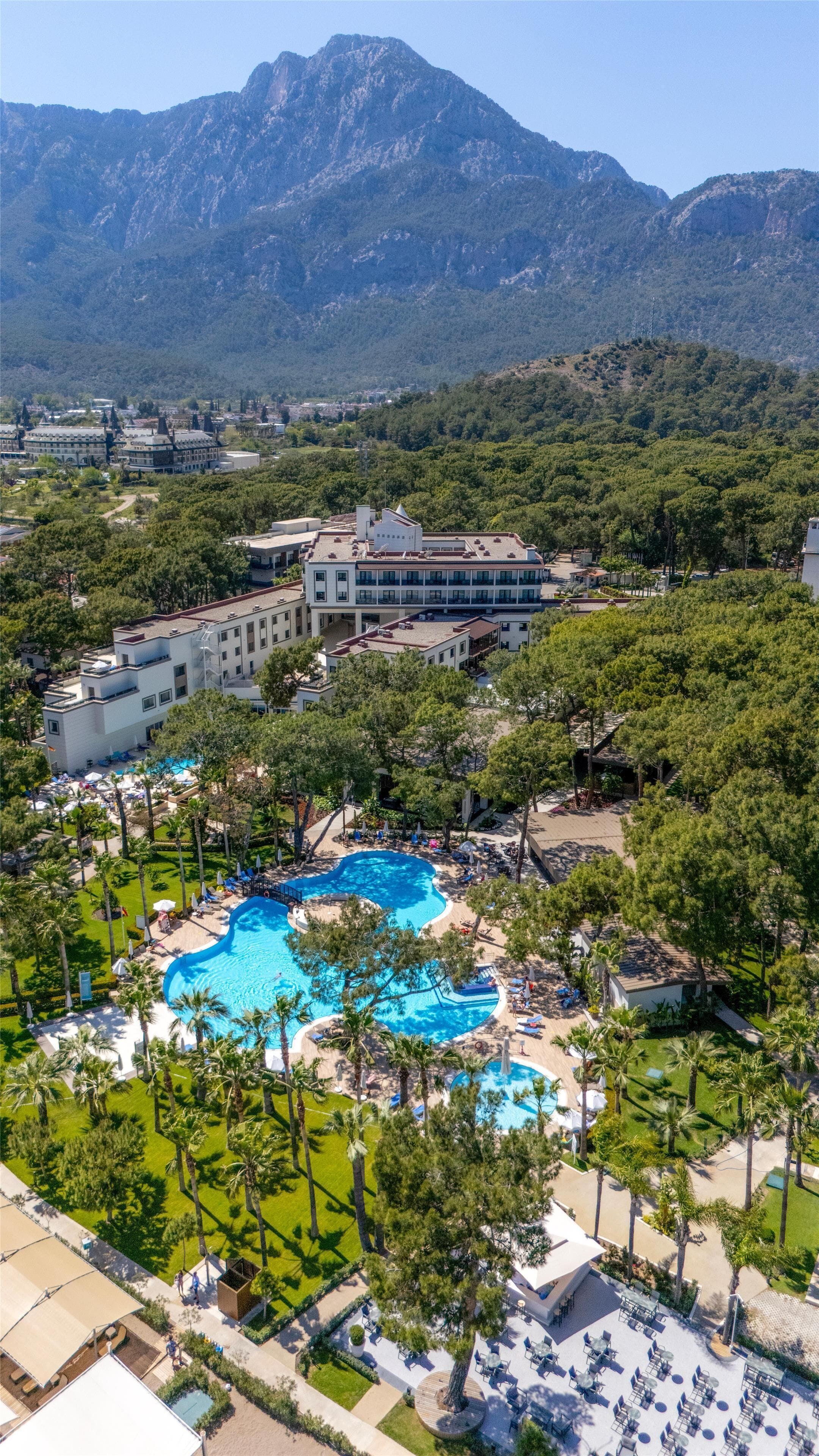 Un resort con varias piscinas, un edificio grande de techo plano y un telón de fondo montañoso.
