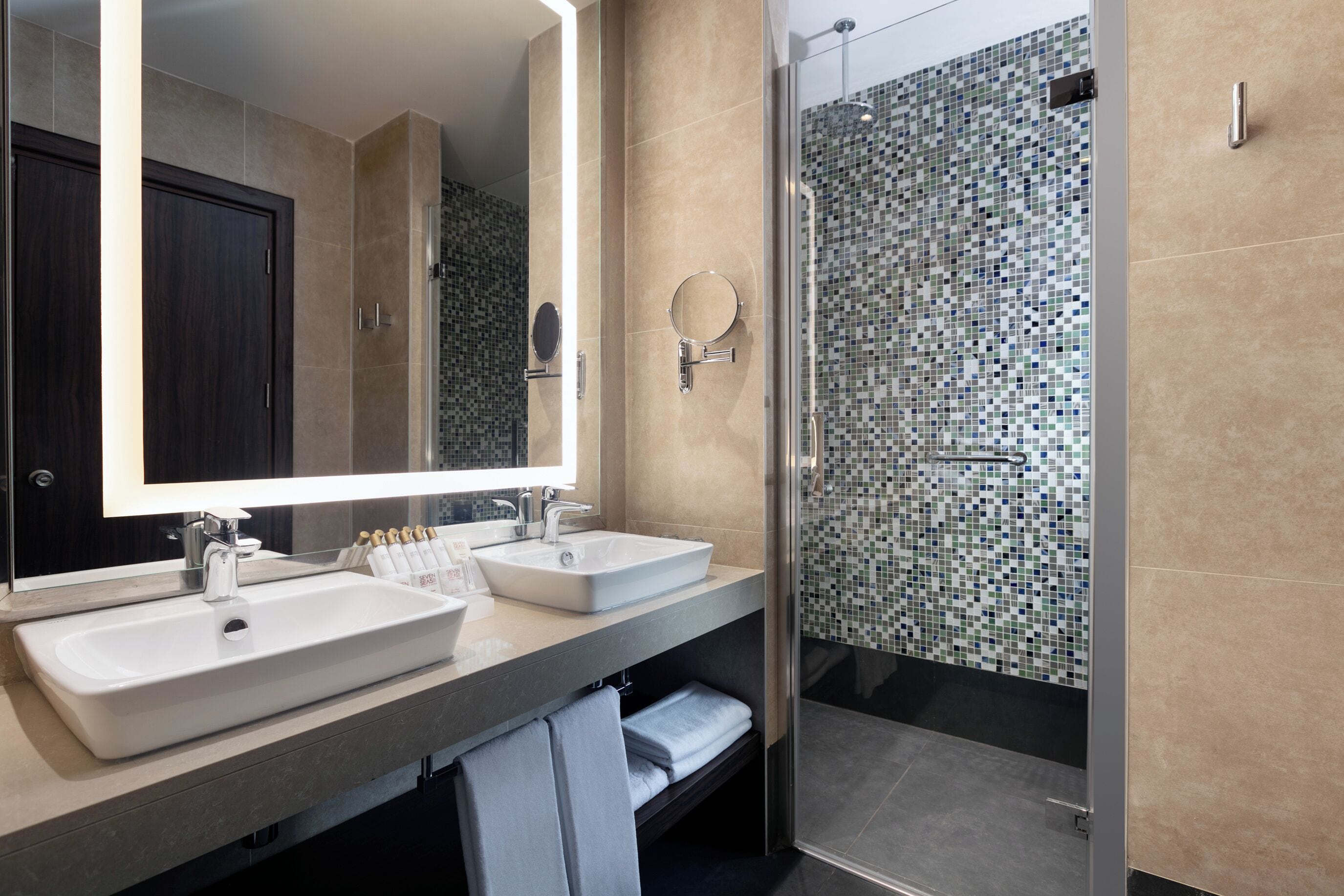 A modern bathroom with two sinks, a large mirror, and a shower with mosaic tiles.