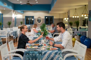Ένας χώρος τραπεζαρίας με τραπέζια στρωμένα για το γεύμα, καρέκλες και έναν ανεμιστήρα οροφής.
