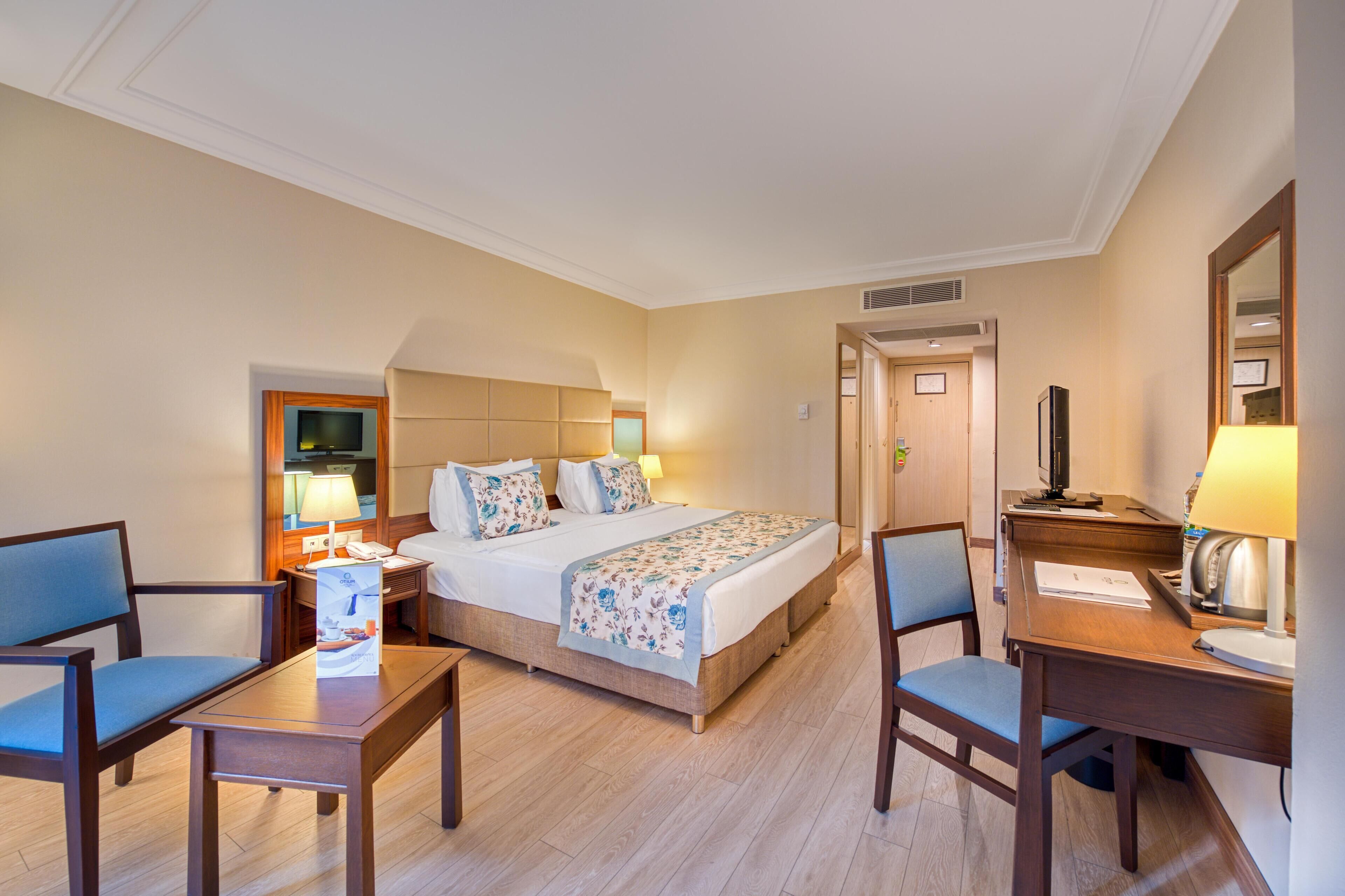 Een hotelkamer met een bed, twee stoelen, een bureau, een televisie en een lamp.