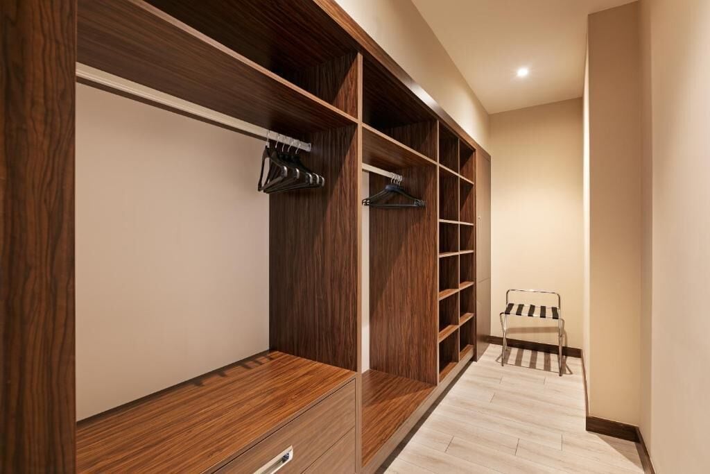 Ein begehbarer Kleiderschrank mit Holzböden und Schubladen, einem Metallstuhl und einem hellen Boden.