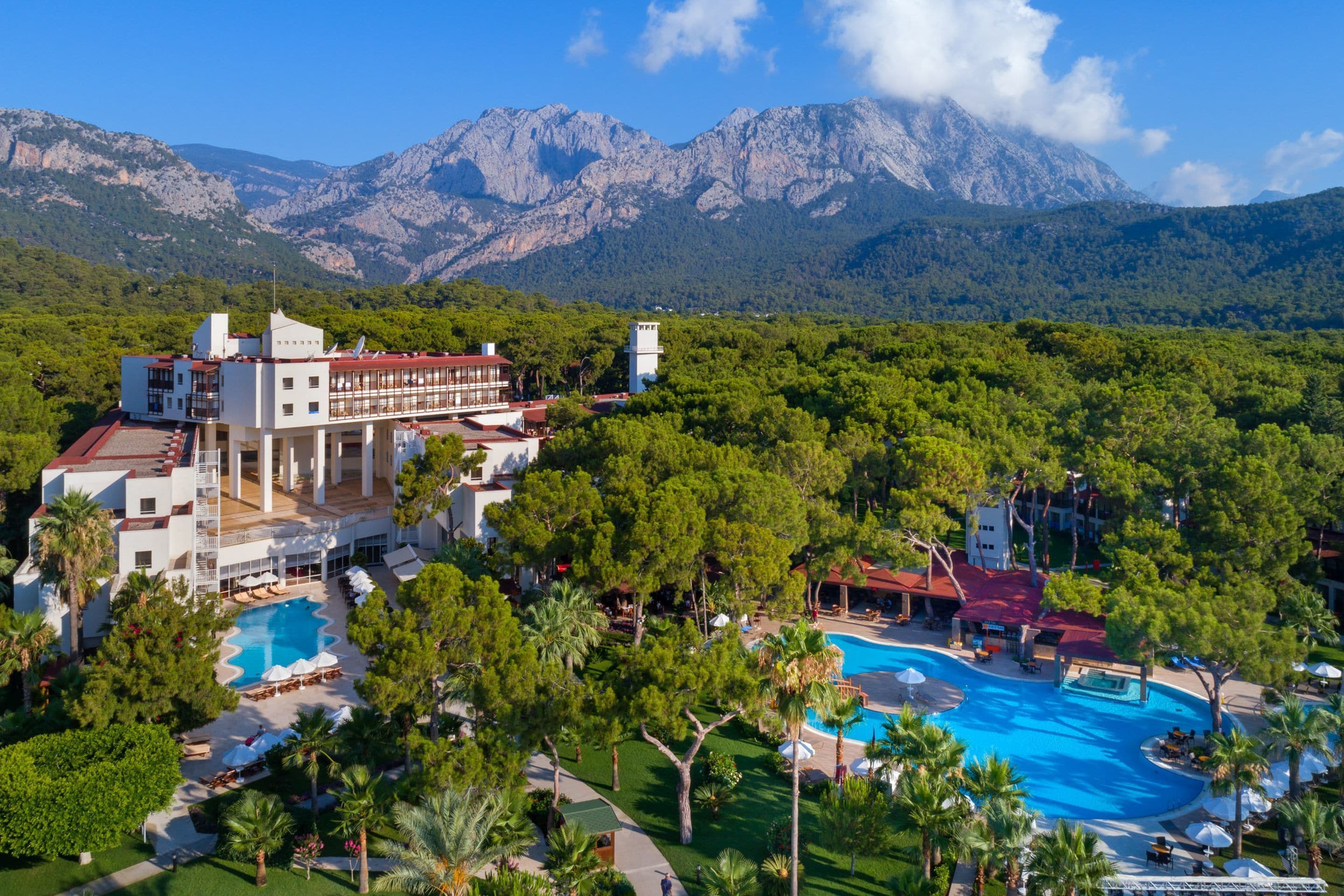Un complejo turístico con varias piscinas, exuberante vegetación y vistas a montañas.