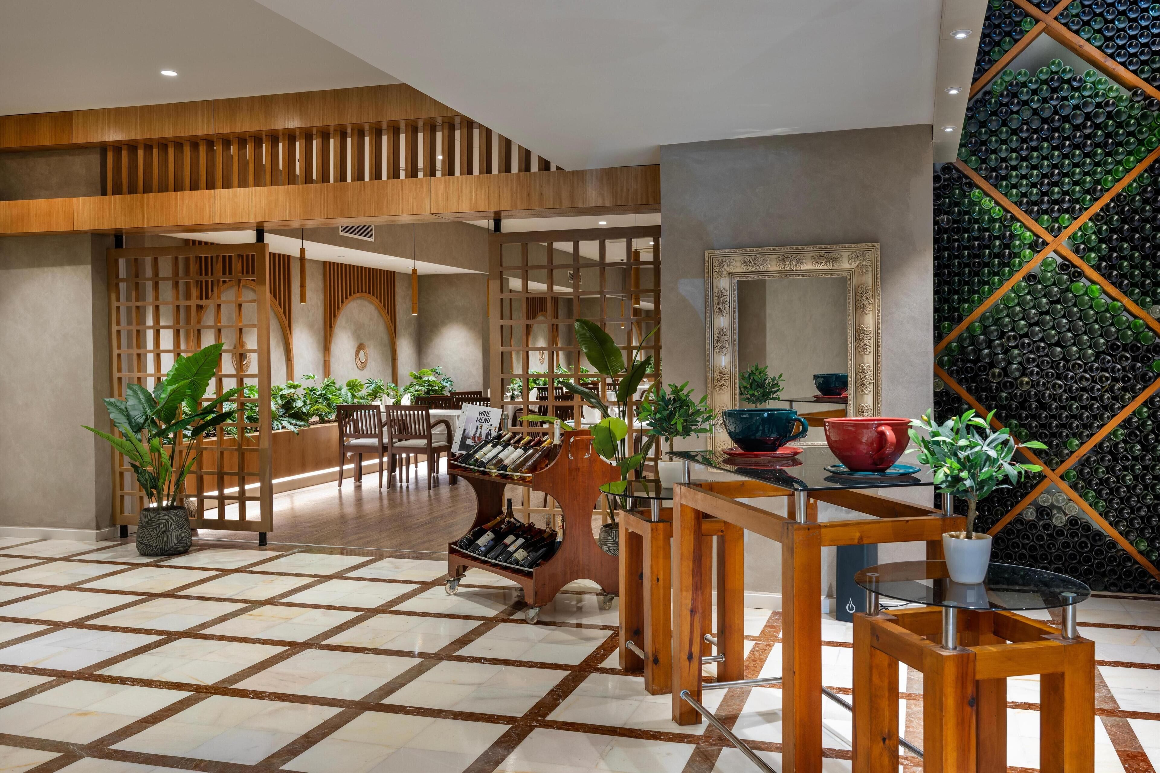 A hotel lobby with a wooden reception desk, a wine rack, and potted plants.