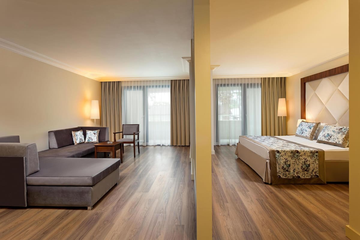 Une chambre d’hôtel avec un canapé, un fauteuil, un lit recouvert d’une courtepointe à motifs floraux et une grande fenêtre avec des rideaux.