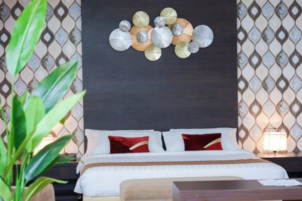 Una cama con ropa de cama blanca y almohadas rojas, un reloj de pared y un adorno decorativo en la pared.