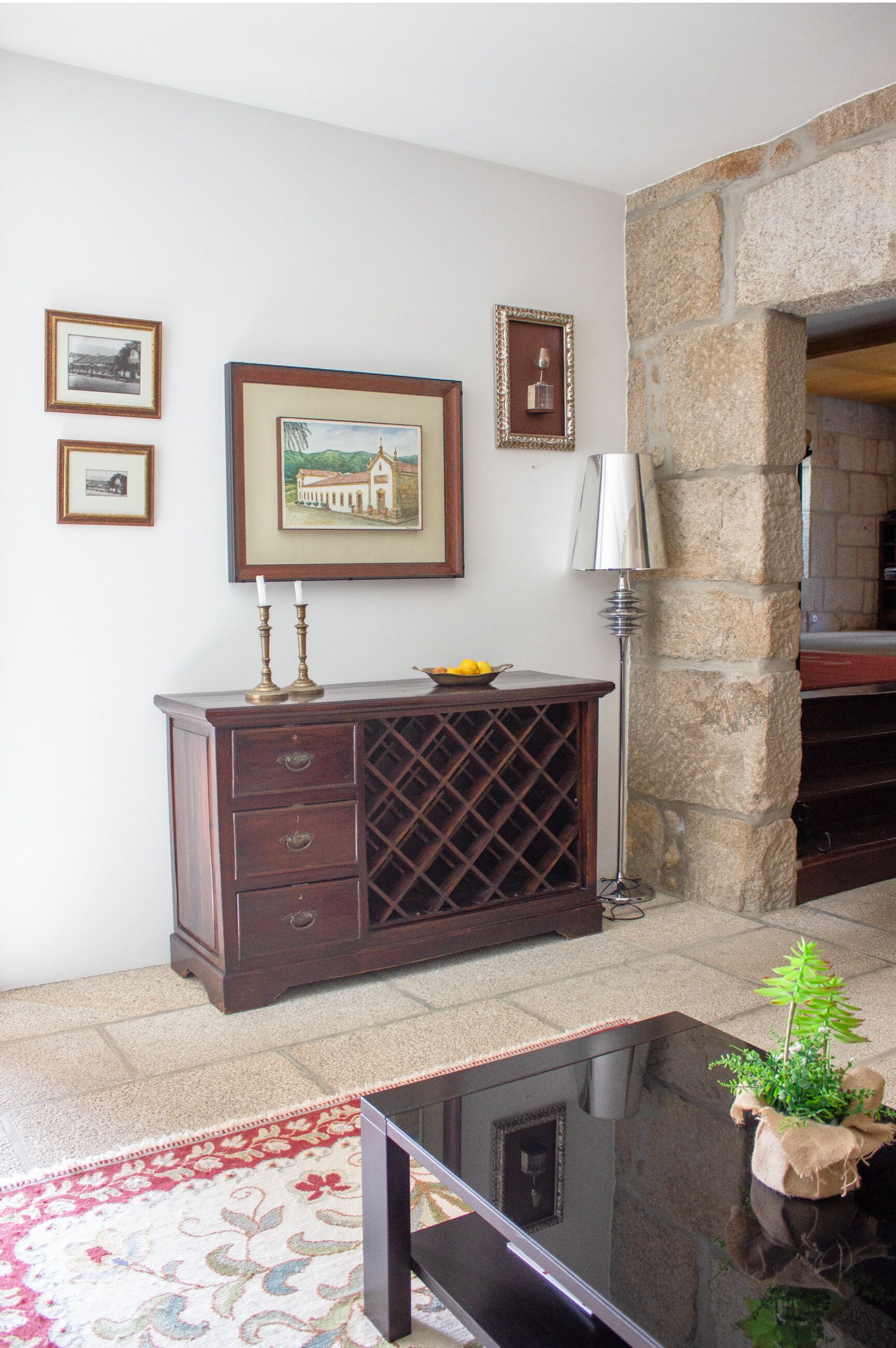 Une pièce avec un meuble en bois, des tableaux encadrés au mur, une table avec une plante et un mur en pierre.