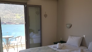 Habitación de hotel con dos camas, un balcón con mesa y sillas, y vista al mar.