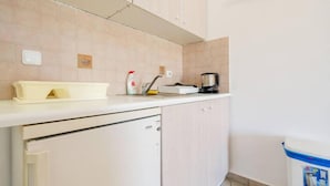 Una cocina con encimera blanca, cafetera y cubo de basura.