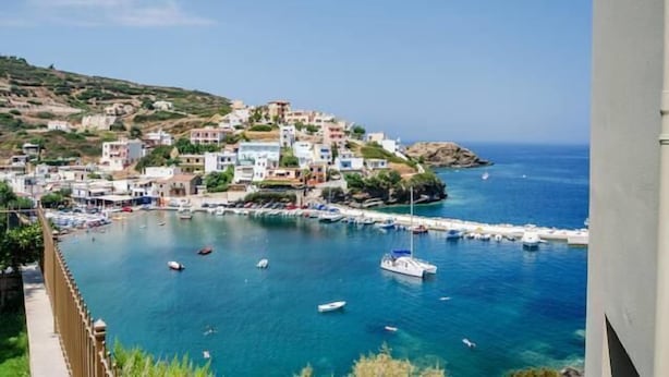 Un pueblo costero con edificios en una colina que dominan un puerto deportivo con barcos.