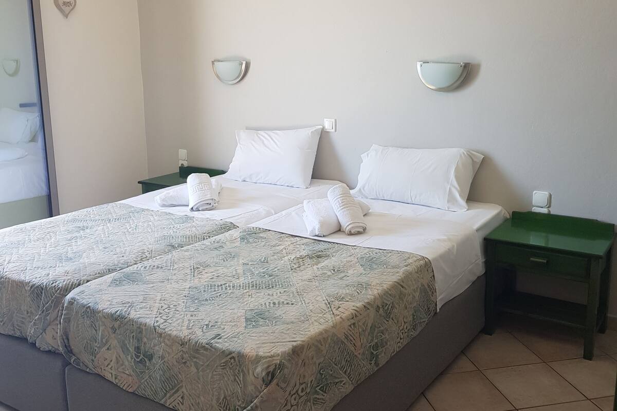 A double bed with white linens, two bedside tables, a wall-mounted air conditioner, and a light fixture.
