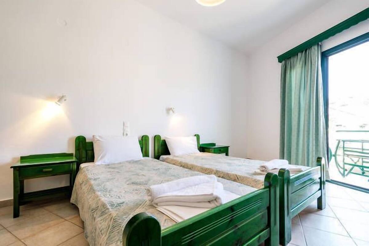 A room with two single beds, a small desk, and a window with curtains.