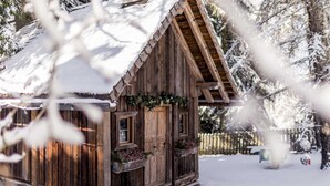 Uma cabana de madeira com telhado coberto de neve, cerca de madeira e chão com neve.