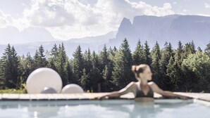 Uma piscina com alguém relaxando, cercada por árvores e montanhas ao fundo.