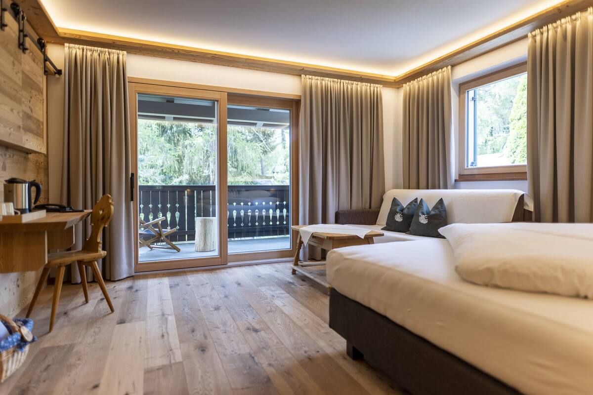 A bedroom with a large bed, a desk, and a chair. There is a sliding glass door leading to an outdoor area.