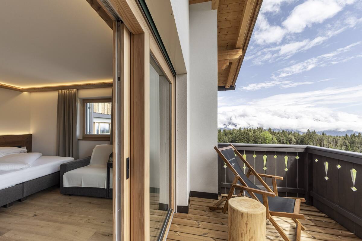 A hotel room with a balcony, a bed, a chair, and a view of the mountains.