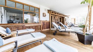 Uma área de spa com piso de madeira, espreguiçadeiras, um balcão de recepção e grandes janelas.