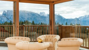 Um deck de madeira com duas poltronas bege e um objeto decorativo dourado, com vista para uma paisagem montanhosa.
