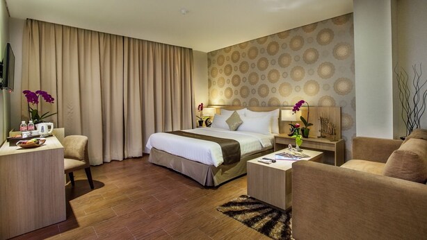 A hotel room with a large bed, a desk, a chair, a sofa, and a decorative wall. - Padjadjaran Suites Resort & Convention (Bogor)