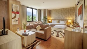 A modern hotel room with a large bed, a sofa, a desk, and a TV. - Padjadjaran Suites Resort & Convention (Bogor)