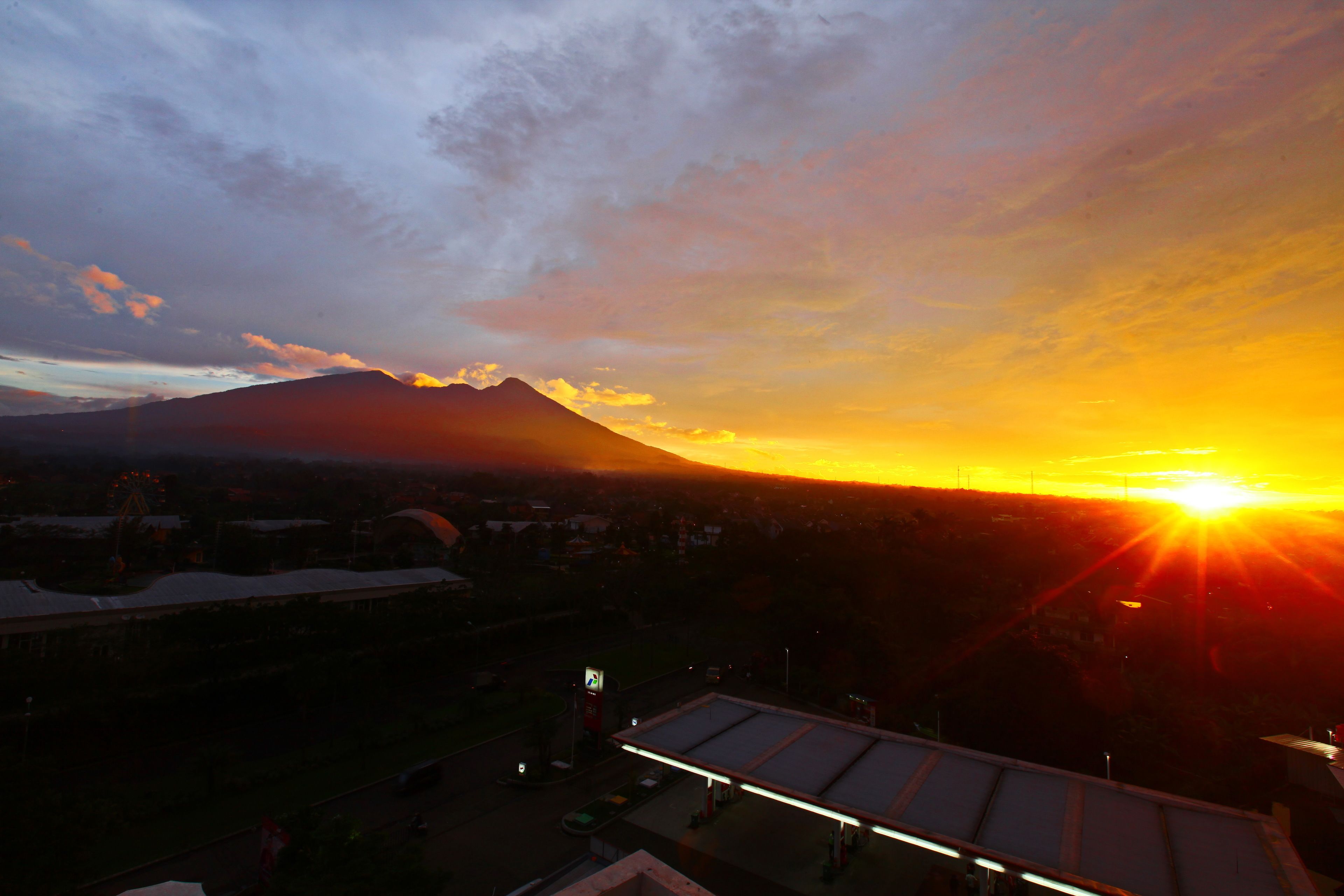 A sunset over a mountain with a gas station in the foreground.