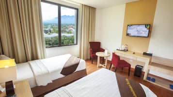 Habitación de hotel con dos camas, un escritorio, una silla, un televisor y una ventana con vistas a una ciudad y montañas.