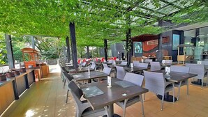 An outdoor restaurant with tables and chairs, a covered seating area, and a view of the surrounding greenery. - Padjadjaran Suites Resort & Convention (Bogor)