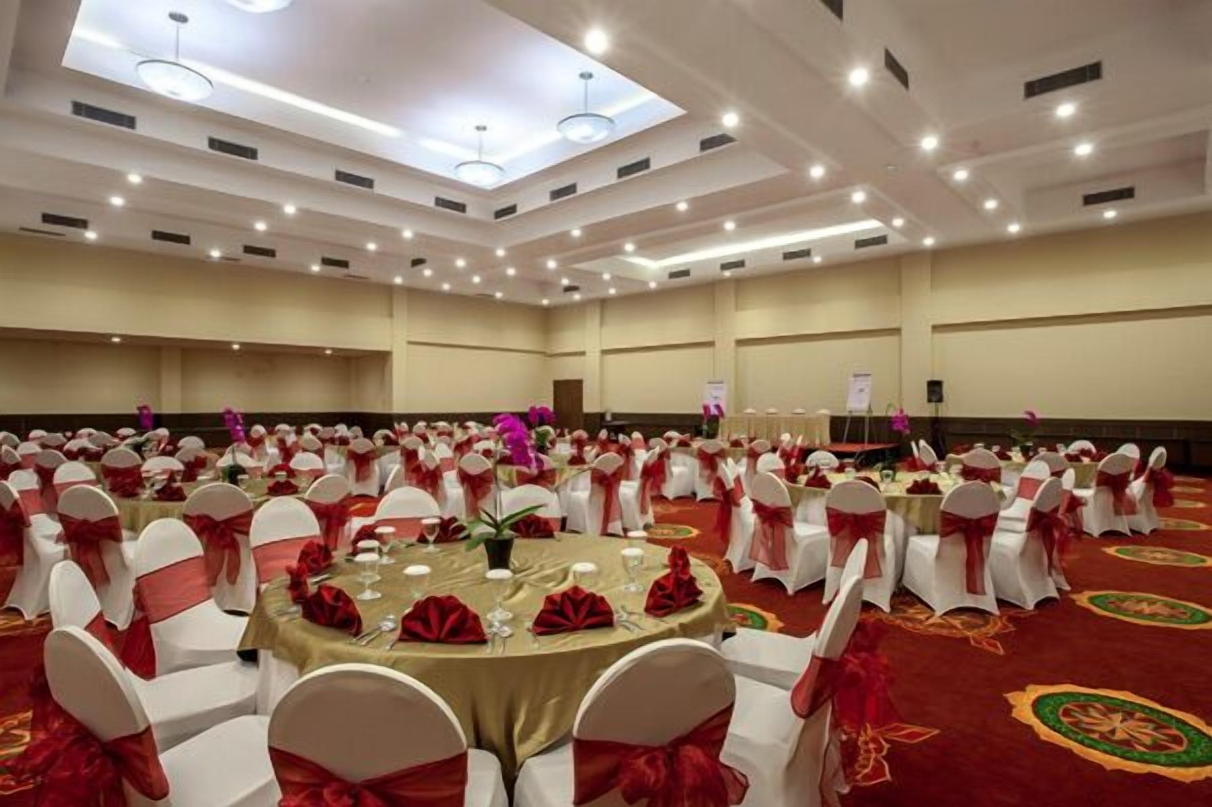 A banquet hall with round tables, white chairs with red sashes, and a red carpet.