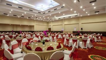 A banquet hall with round tables, white chairs with red sashes, and a red carpet.