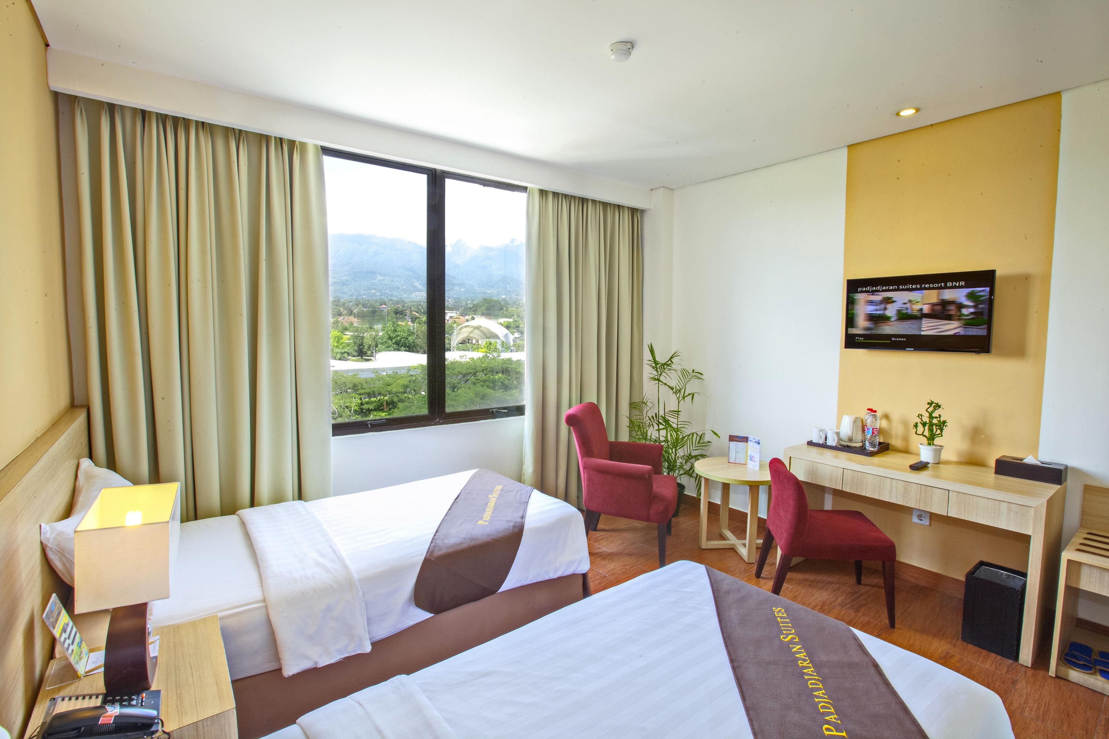 A hotel room with two beds, a desk, a chair, a television, and a view of mountains.