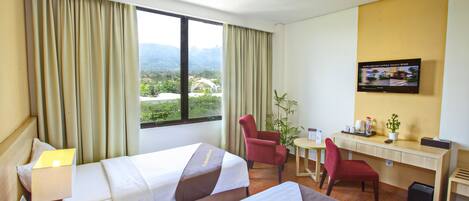 A hotel room with two beds, a desk, a chair, a television, and a view of mountains.